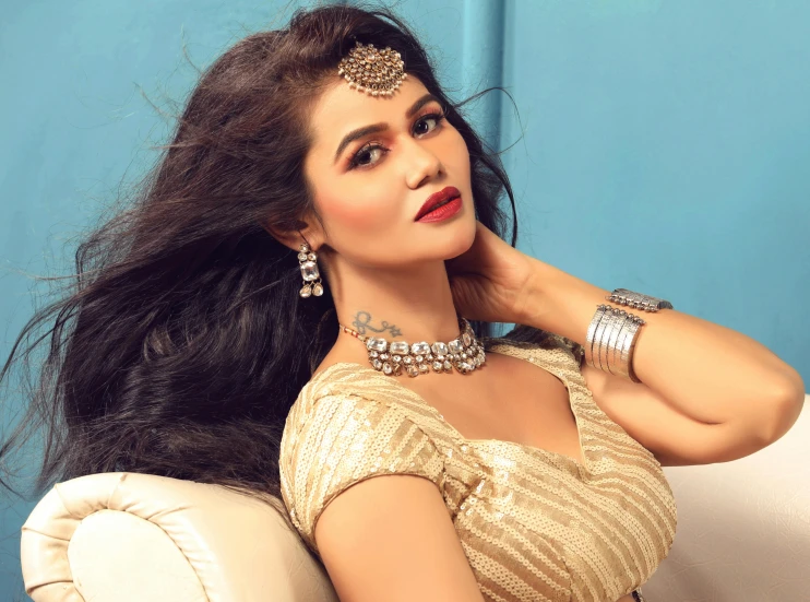 a woman in a golden dress wearing jewellery sits down