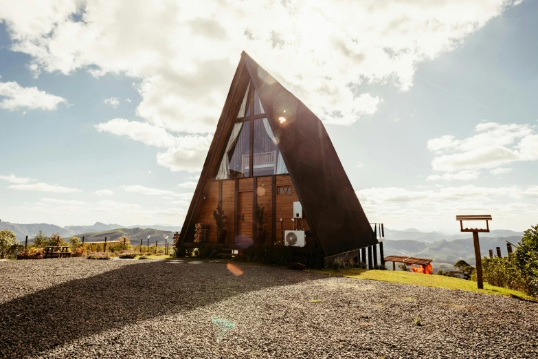 a triangular shaped wooden house sitting on a gravel road