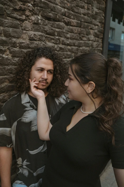 two people standing next to each other near a stone wall