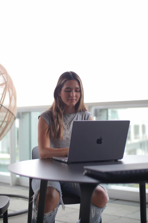 a woman in grey shirt using laptop computer at table