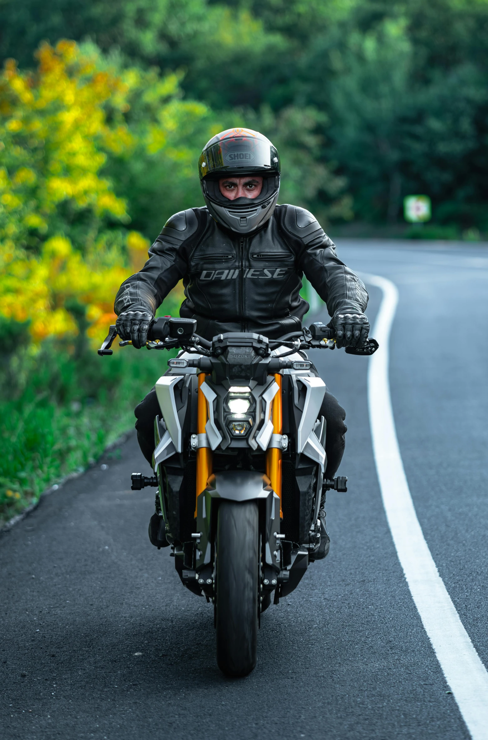 a man with helmet and leather gear riding a motorcycle down a road