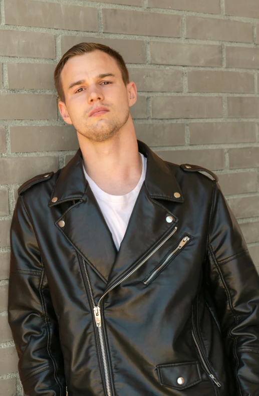 a man in a black jacket standing near a brick wall