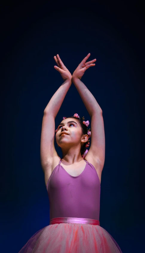 a girl in a pink dress standing and reaching her arms up