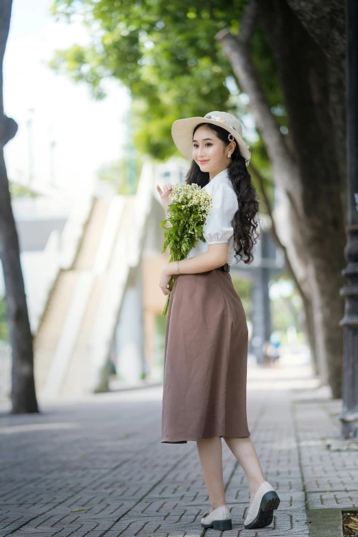 a woman holding a flower while wearing a hat