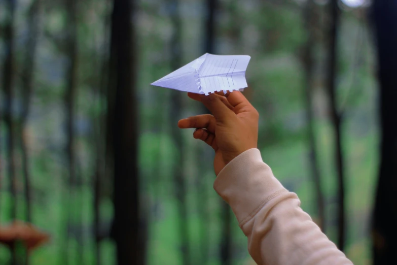 an asian woman is holding up a white origami bird in front of her