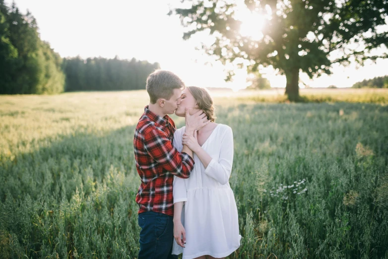 an engaged couple is hugging in a field with trees