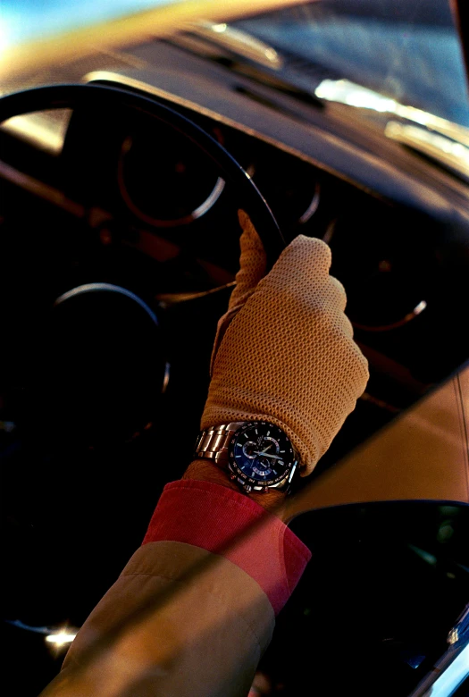 a hand on a car steering wheel with an orange and black striped glove