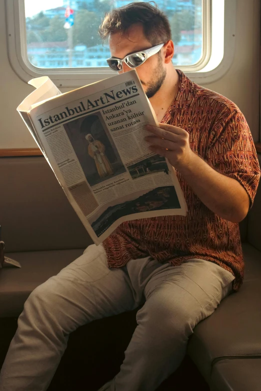 a man wearing glasses sitting on a bench reading a newspaper