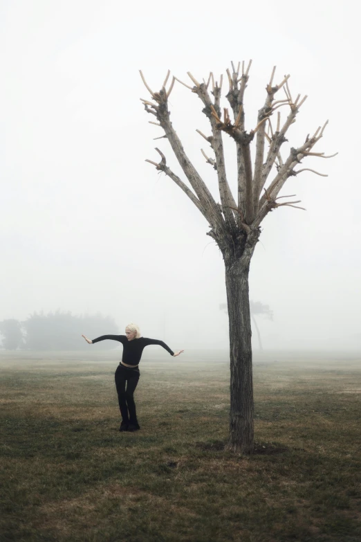 a woman is standing by a tree in a foggy field