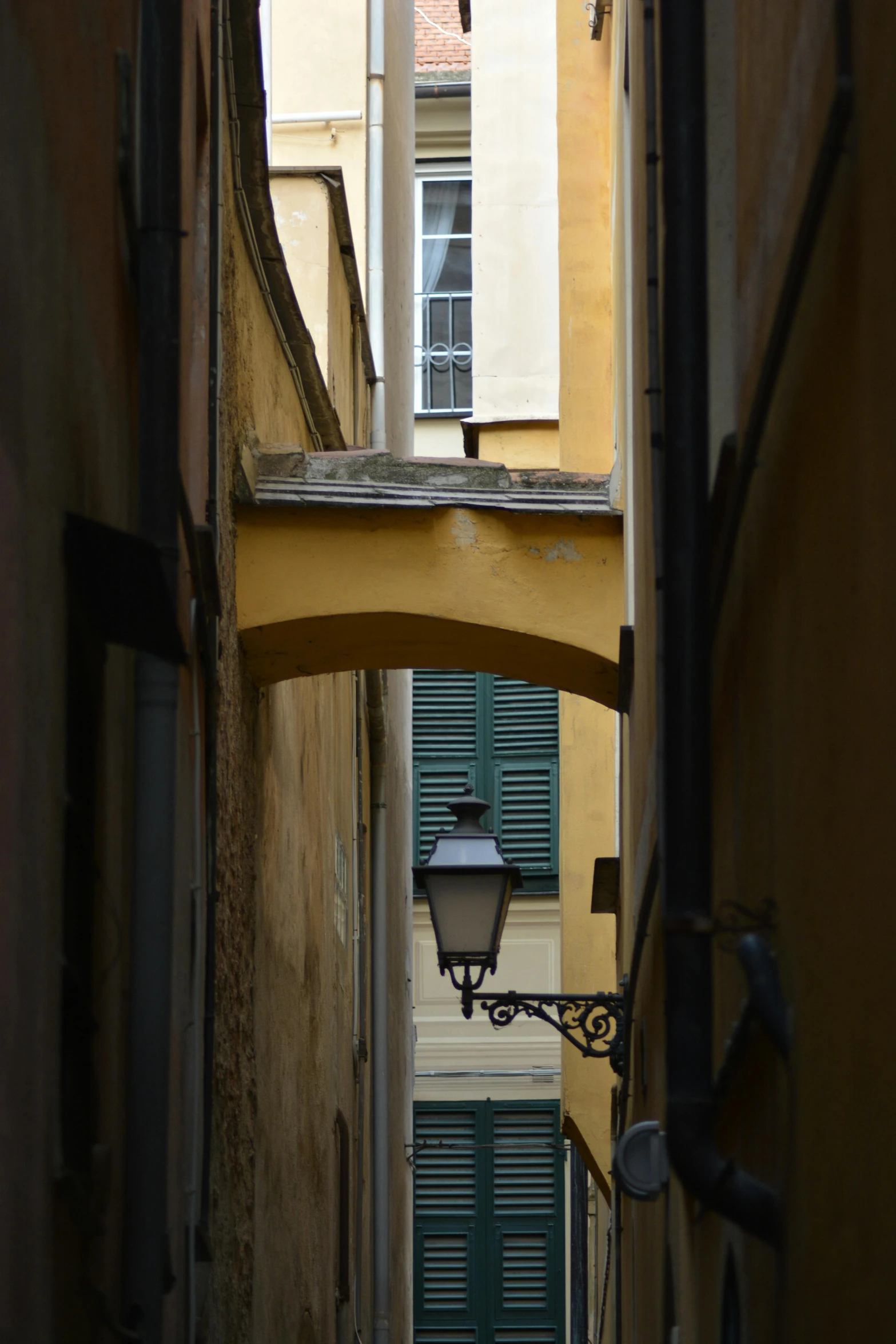 view down an alley between buildings with shutters and a street lamp