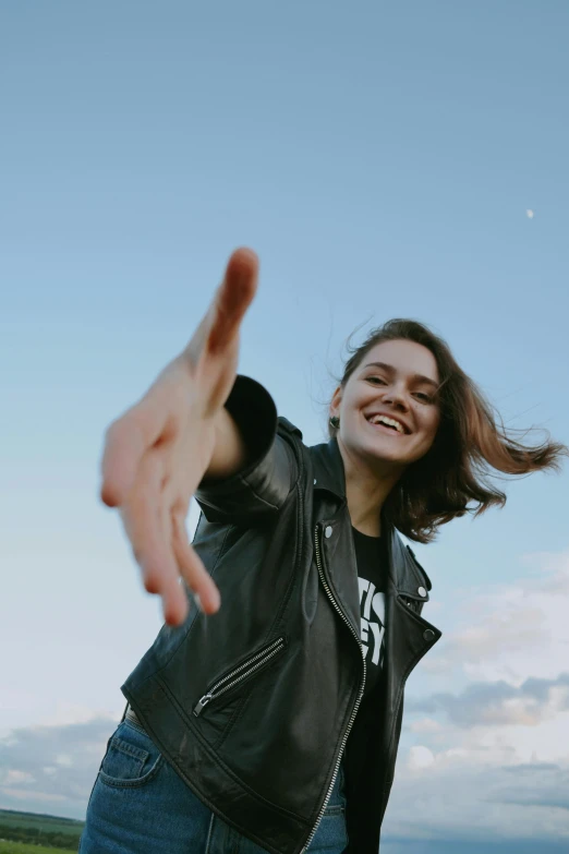 a woman wearing jeans and a jacket reaching her hand up towards the sky