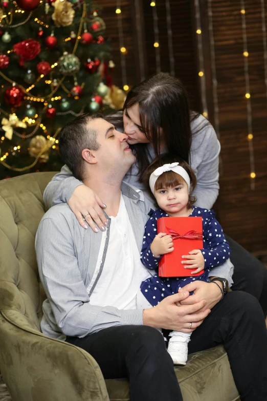 a family of three sitting next to a christmas tree