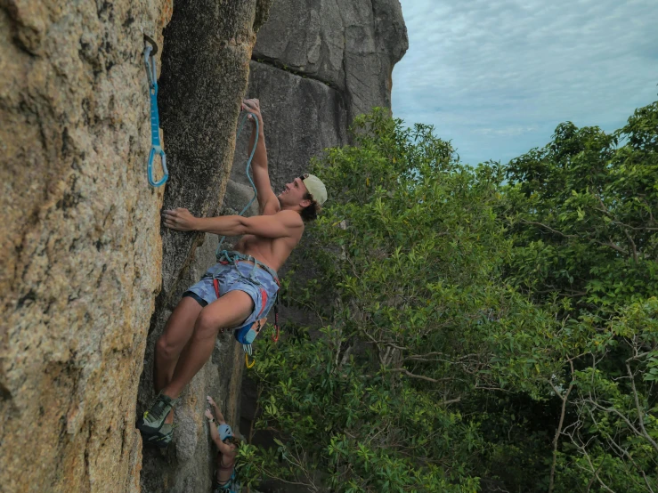 the man is climbing up a cliff with a hat on