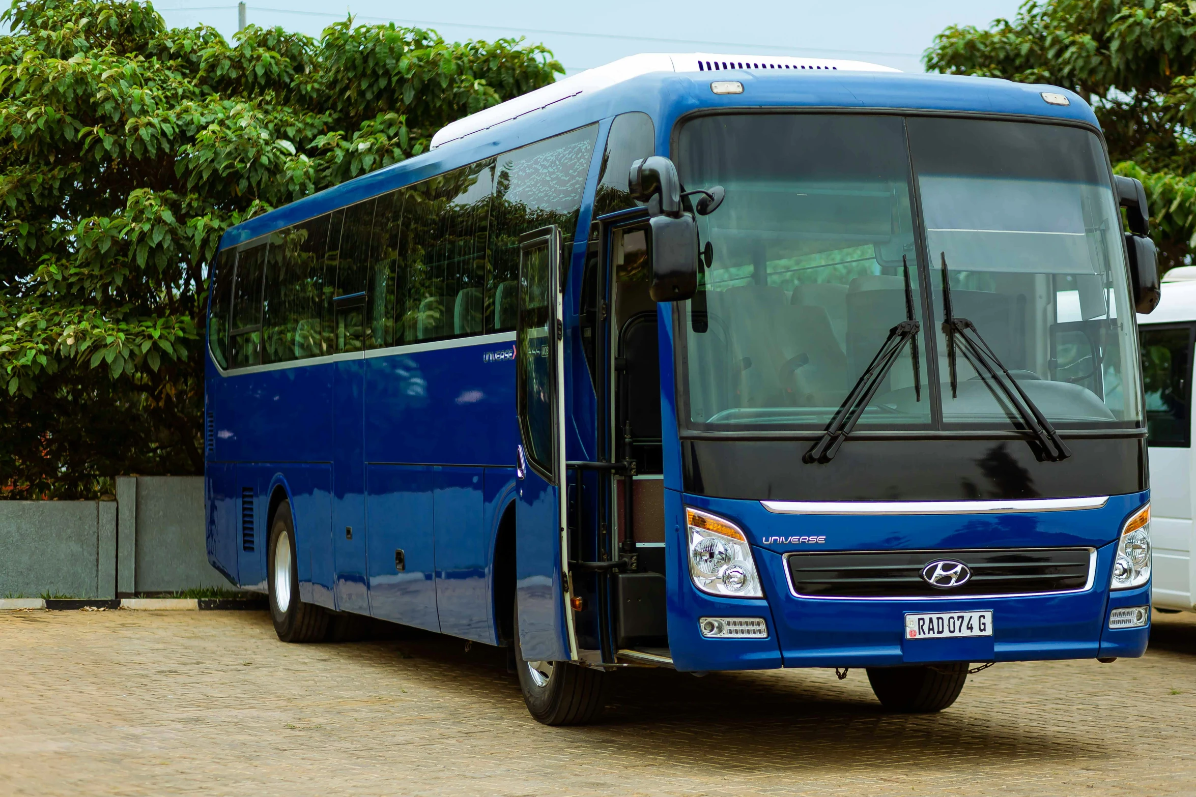 the blue bus is parked near trees and a fence