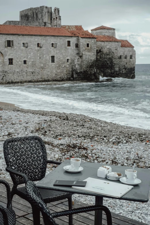 a table and chairs near the ocean facing a castle