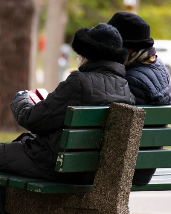 two people sitting on a green park bench