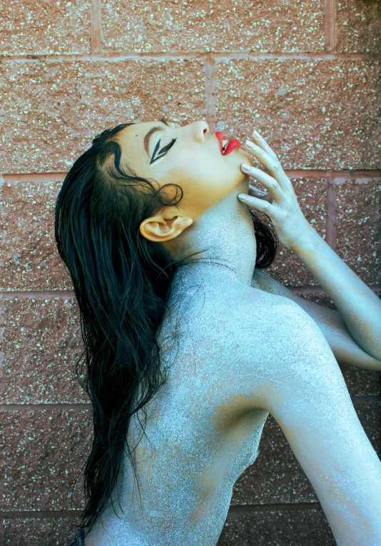 woman with glittery skin posing by a brick wall