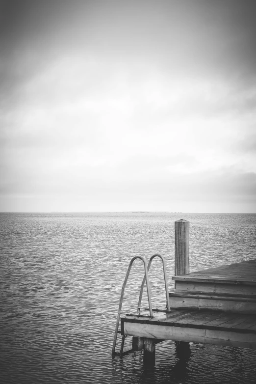 a black and white pograph of the water by a pier