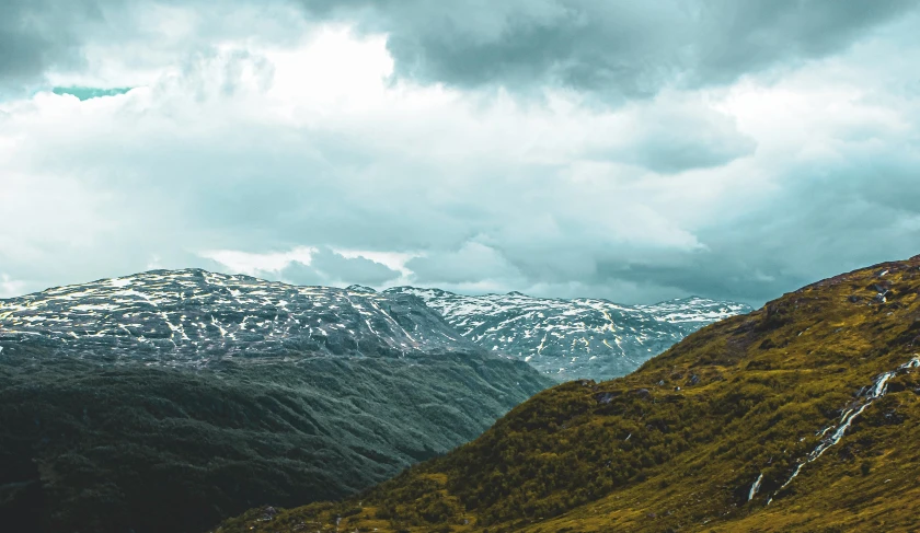 snowy mountains under cloudy skies with sp trees