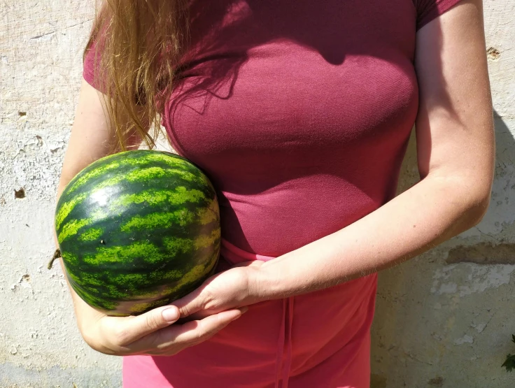 a woman holding onto a watermelon in front of a wall