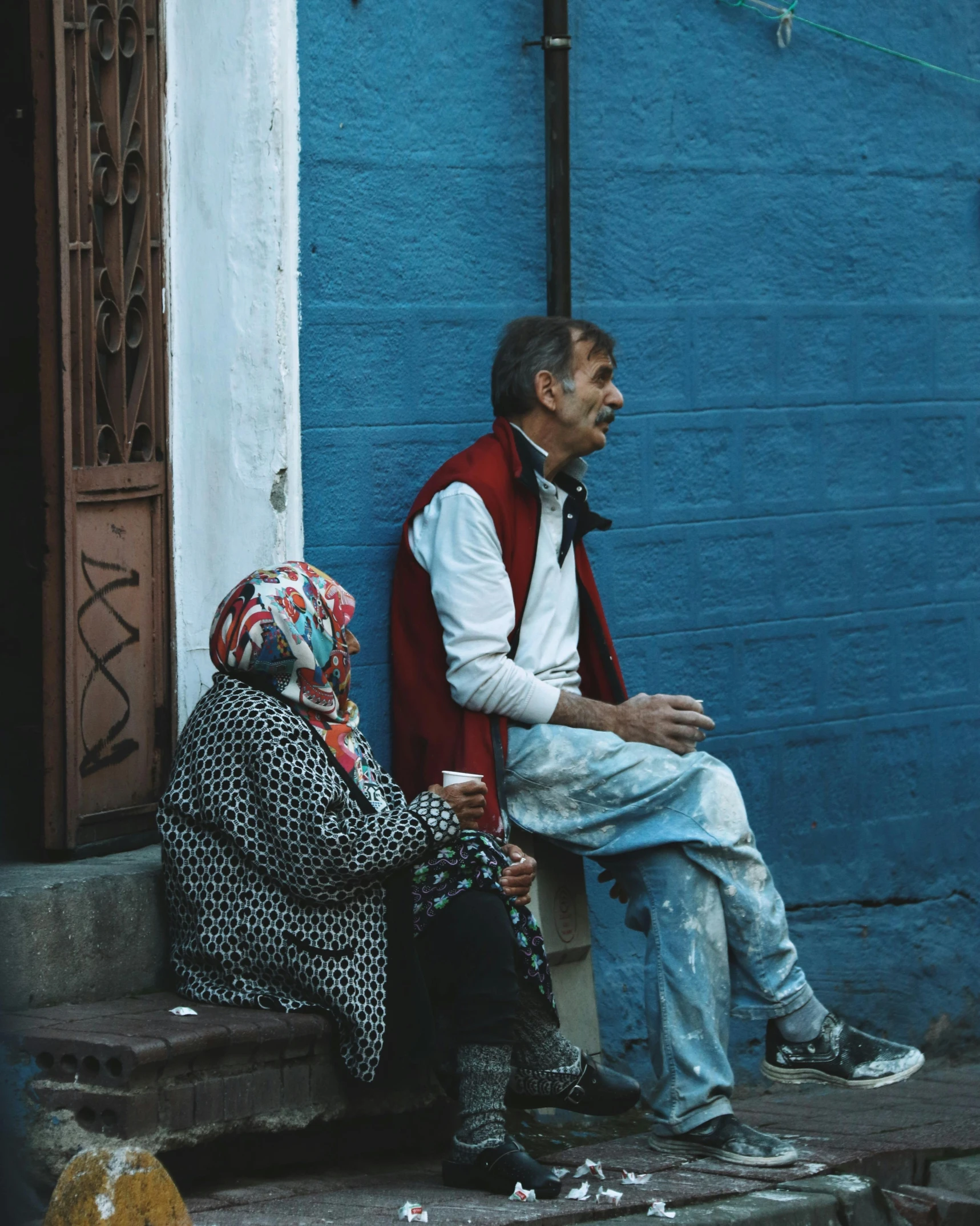 two people are sitting on the curb of a building