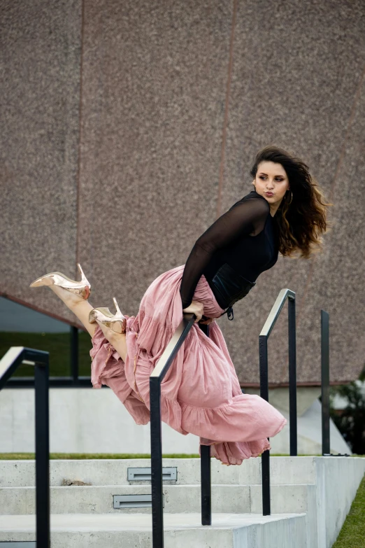 a woman in black top and pink skirt leaning against stairs