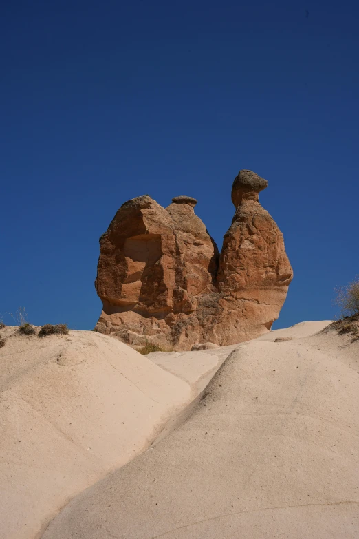 two rocks sticking out of sand with a blue sky in the background