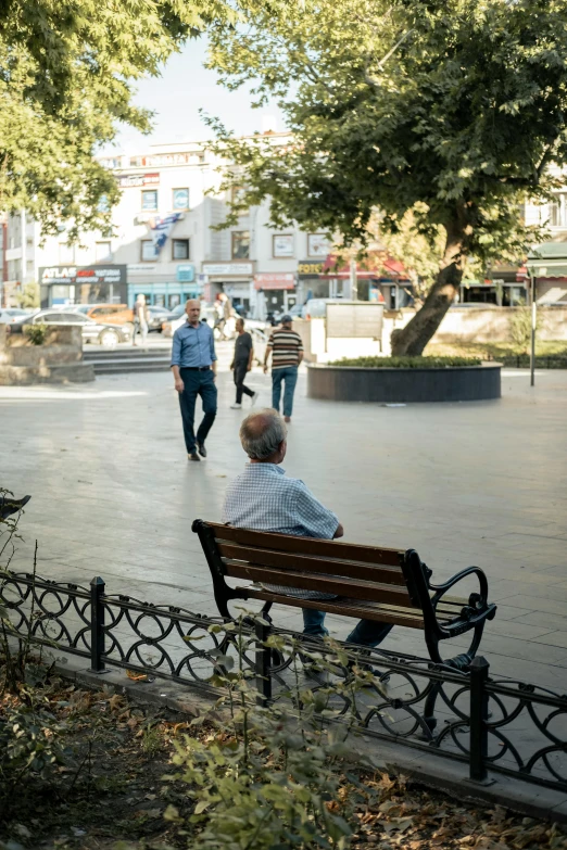 a man sitting on top of a wooden bench next to a tree