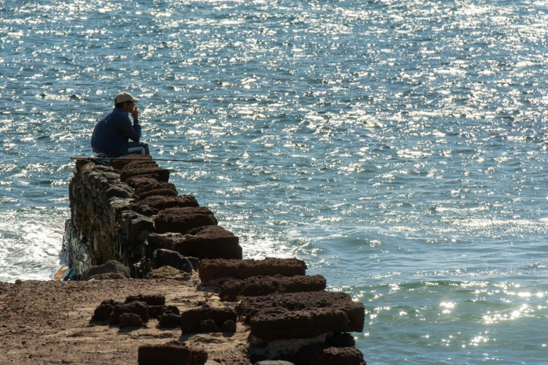man sitting on the edge of a pier near the ocean