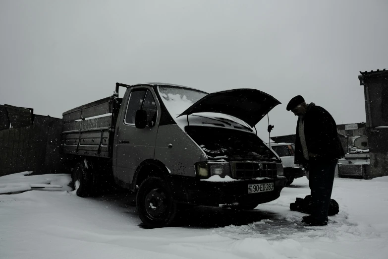 two men work on a car in the snow