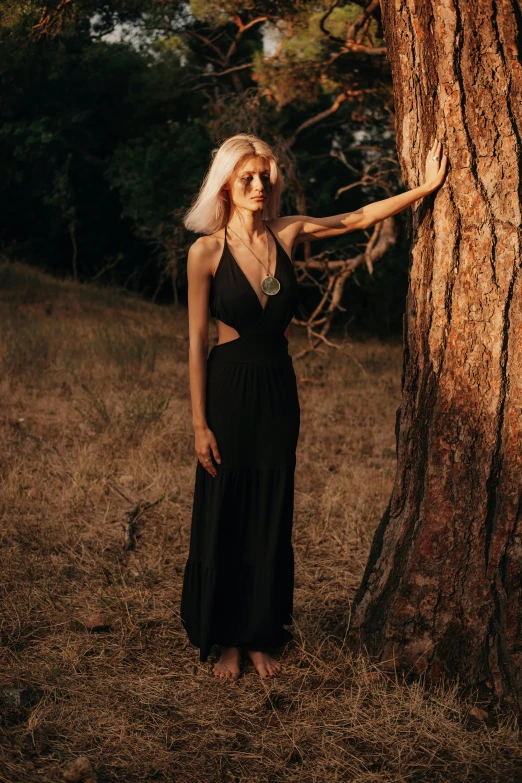 the blond woman is standing in the woods by a tree