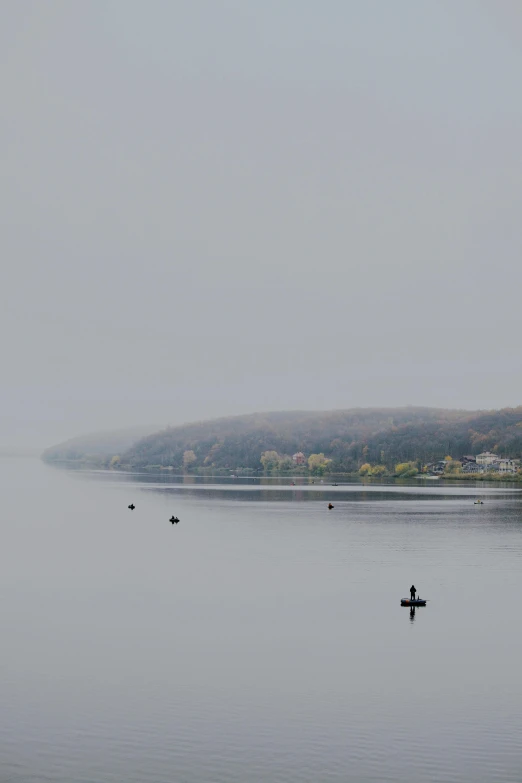 two people floating in the middle of a lake with trees and a hill in the background