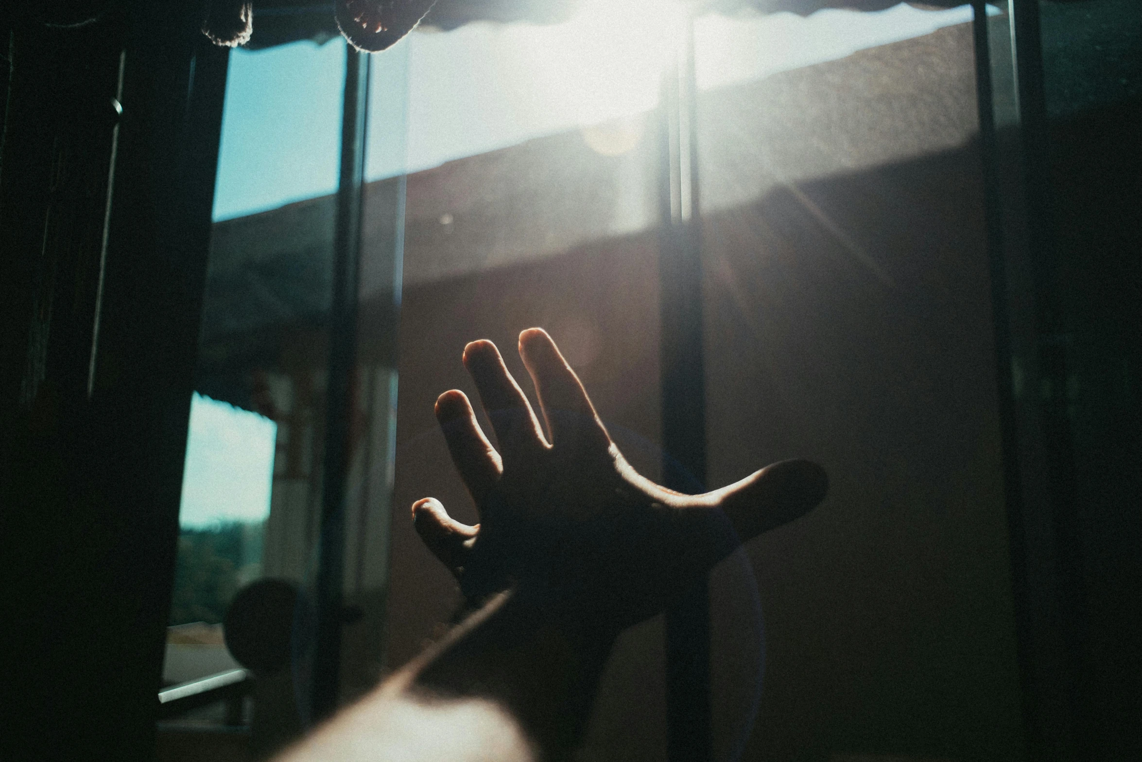 a hand reaching out from a window with the sun shining on it