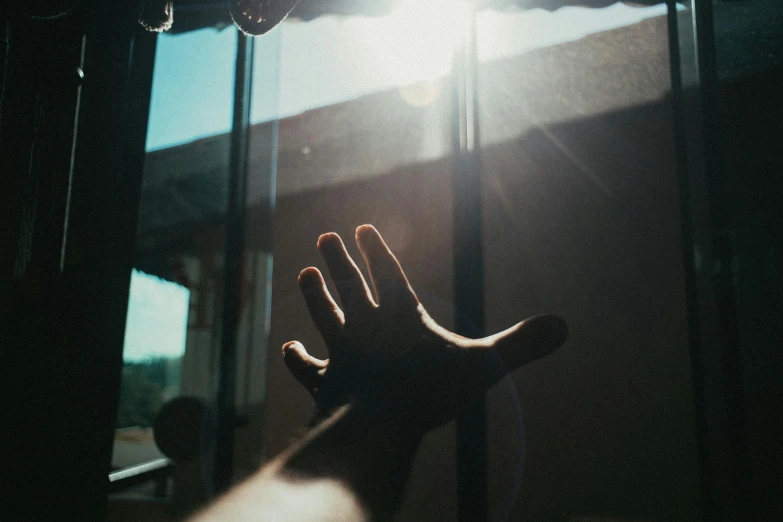 a hand reaching out from a window with the sun shining on it