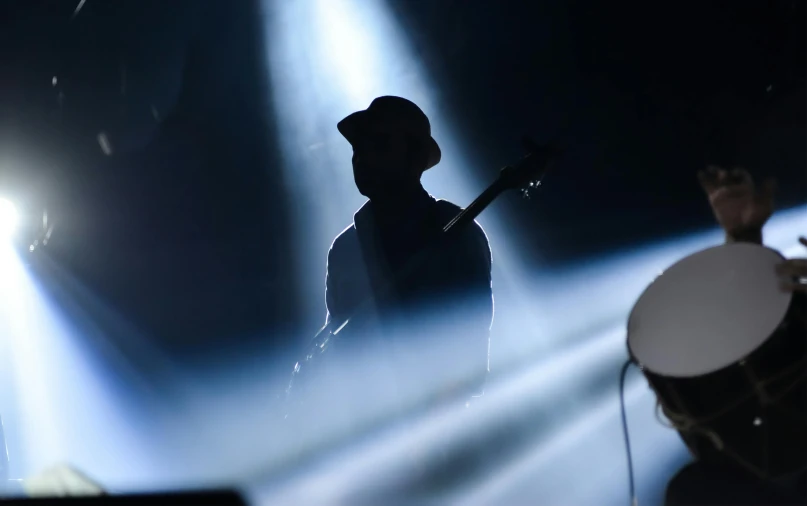 silhouetted musician standing on stage with light coming from the back