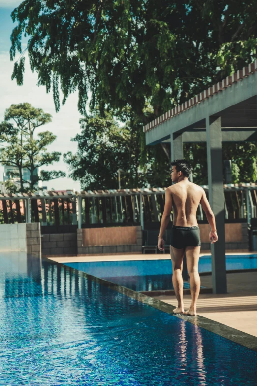 a man standing next to a pool wearing a black swimsuit