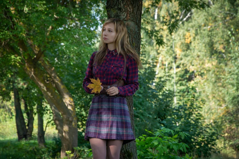 a girl is wearing a red plaid coat, holding flowers while standing against a tree