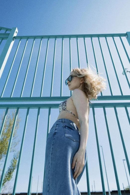 a woman in sunglasses and a skirt by some green fence