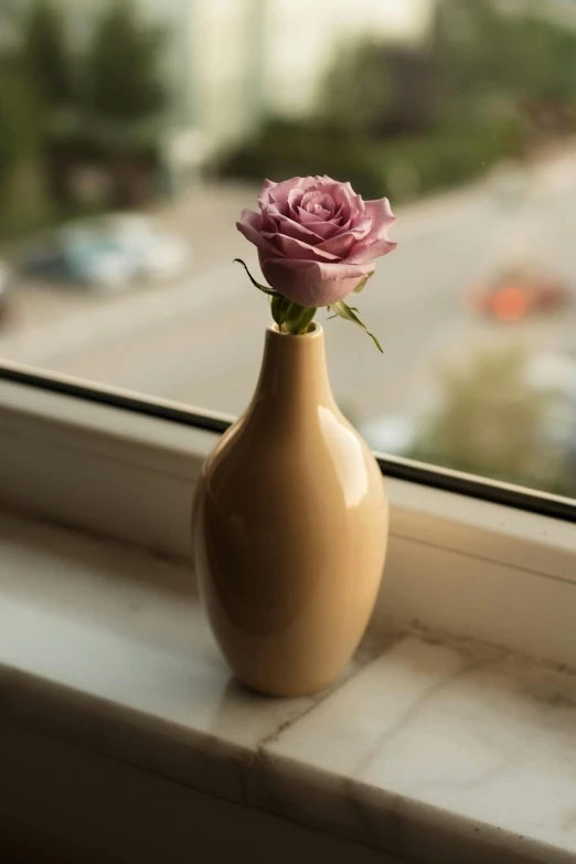 a tan vase is holding a pink rose