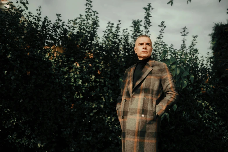 a man in a plaid coat leaning on some bushes