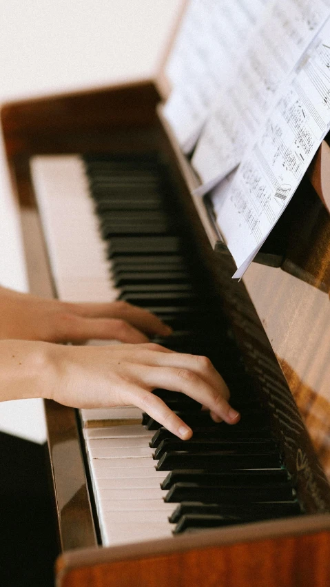 hands on an old, wooden piano and sheet music