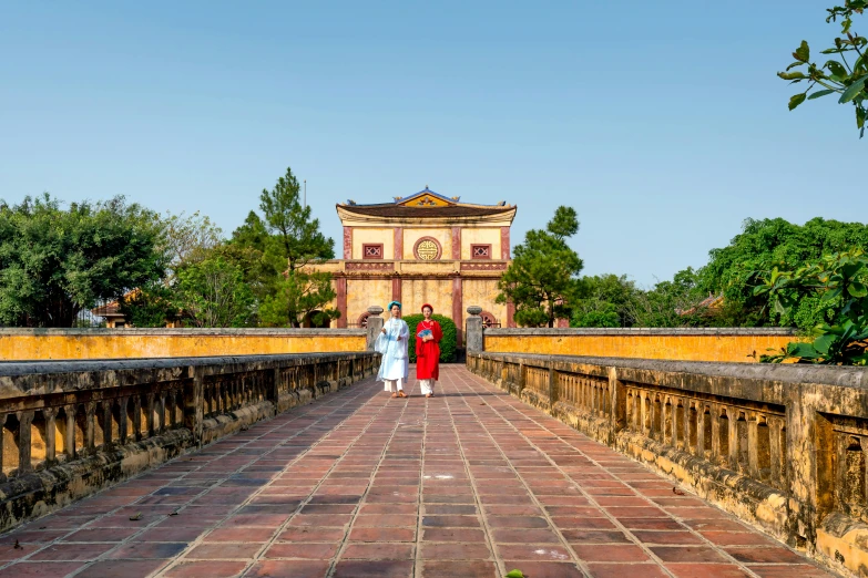 two women standing on a bridge that has an old building in the background