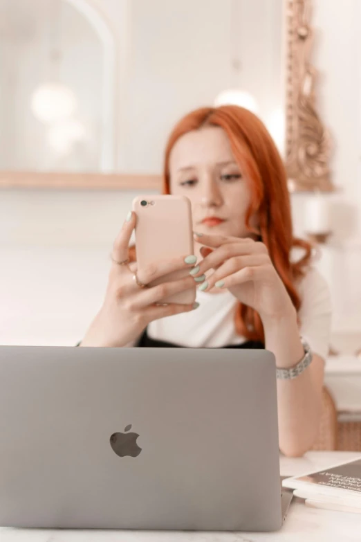 a red headed woman using a laptop computer and her cellphone