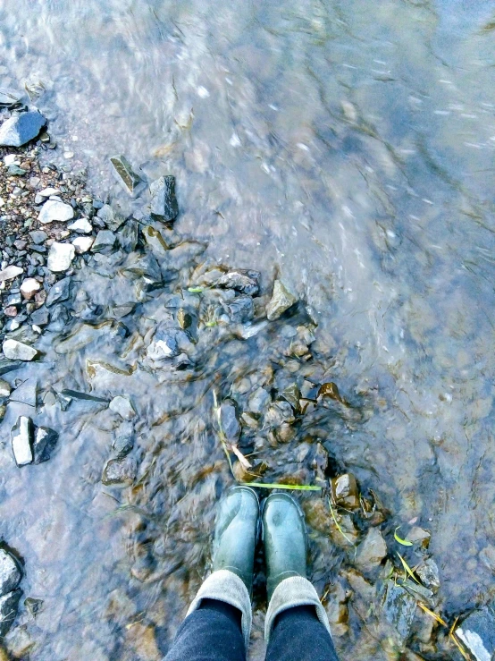 a person is standing next to the water on rocks and grass