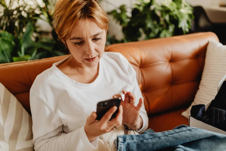 woman on couch using cell phone while sitting next to plant