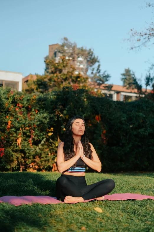 a woman is meditating in the middle of a lawn