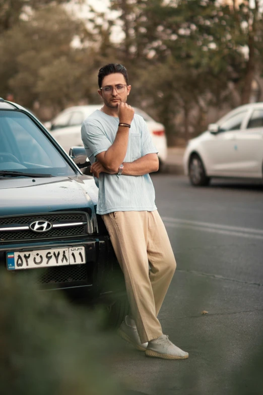 a man in khaki stands next to a car on the side of a road