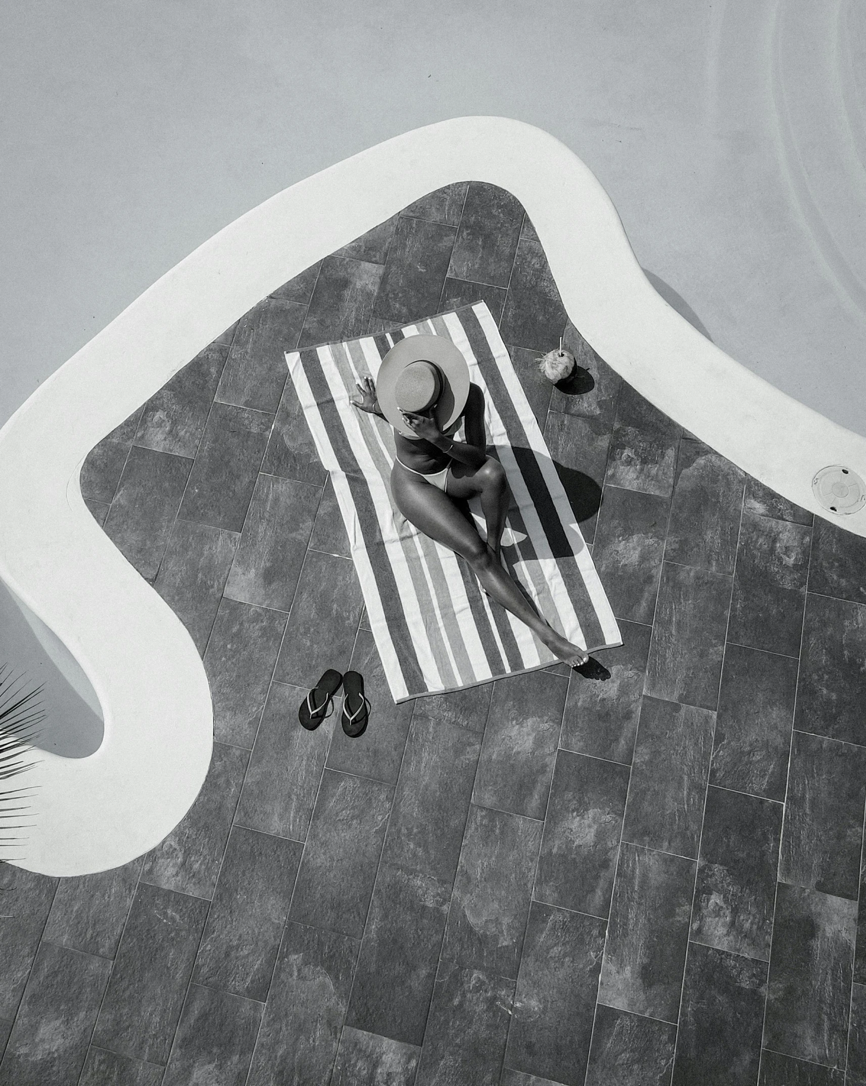 an aerial s of a woman in bathing suit and white hat sitting at a swimming pool