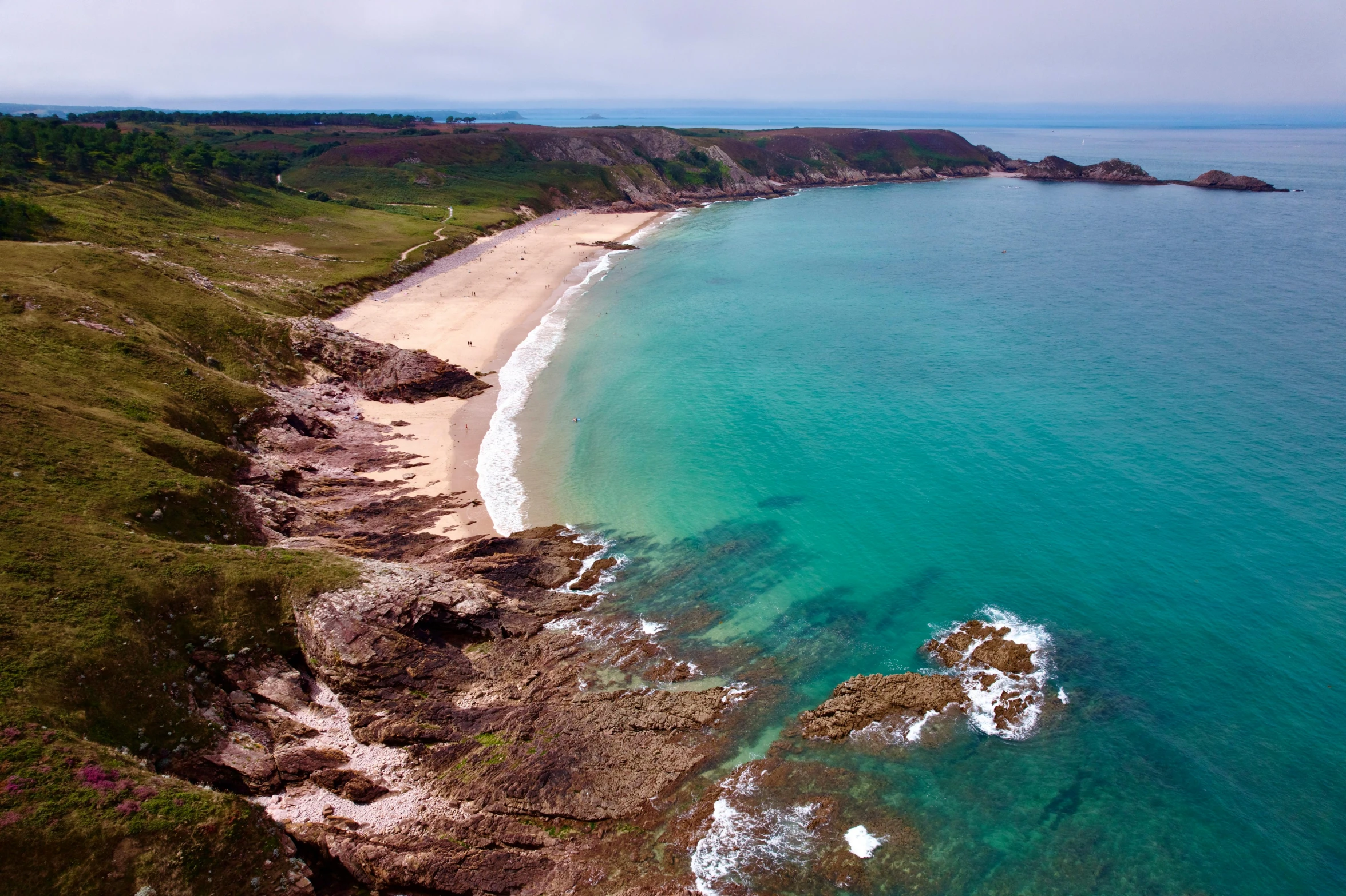 the aerial view shows a sandy beach, large body of water and green hills