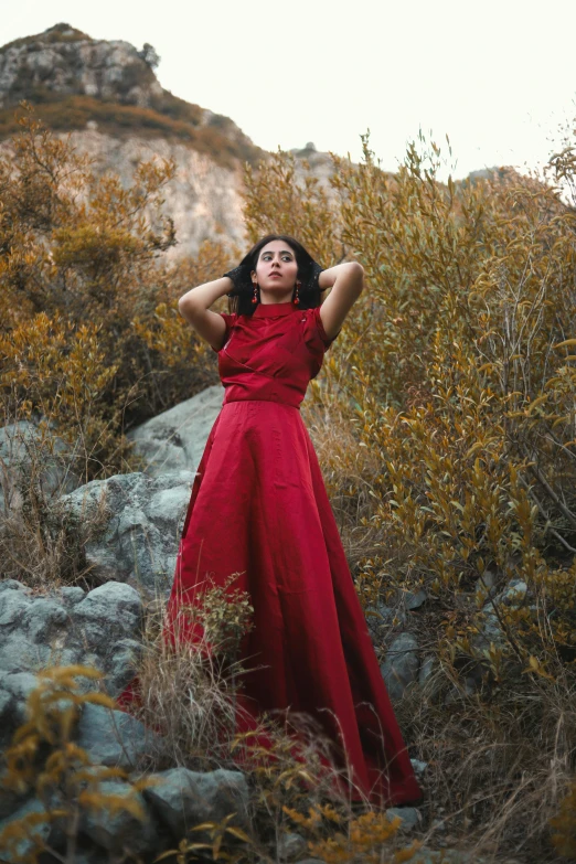 a woman wearing a red dress stands in the wilderness